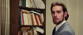 Movie still from “What Have You Done to Solange?” (1972), directed by Massimo Dallamano – A person wearing a suit and tie in front of a book shelf; Close Up shot, Over the shoulder angle