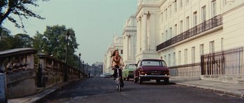 Movie still from “What Have You Done to Solange?” (1972), directed by Massimo Dallamano – A woman riding a bike down a street past tall buildings; Extreme Wide shot, Low angle