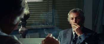 Movie still from “What Have You Done to Solange?” (1972), directed by Massimo Dallamano – An older man smoking a cigarette while sitting at a table; Close Up shot, Over the shoulder angle