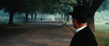 Movie still from “What Have You Done to Solange?” (1972), directed by Massimo Dallamano – A man wearing a black hat and a white shirt is standing in a park; Wide shot, Over the shoulder angle