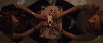 Movie still from “What Lies Beneath” (2000), directed by Robert Zemeckis – A group of people sitting at a table with a ouija board on it; Medium shot, Overhead angle