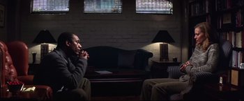 Movie still from “What Lies Beneath” (2000), directed by Robert Zemeckis – A man sitting on a couch in a living room; Medium shot, Over the shoulder angle