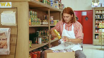 Movie still from “What's Eating Gilbert Grape” (1993), directed by Lasse Hallström – A man in an orange and white striped shirt putting food into a box; Medium shot, Low angle