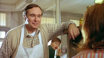 Movie still from “What's Eating Gilbert Grape” (1993), directed by Lasse Hallström – A man in an apron leaning against a counter; Medium shot, Over the shoulder angle