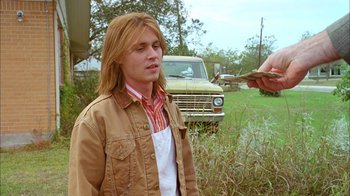 Movie still from “What's Eating Gilbert Grape” (1993), directed by Lasse Hallström – A young man in a field holding a knife in his hand; Medium shot, Over the shoulder angle