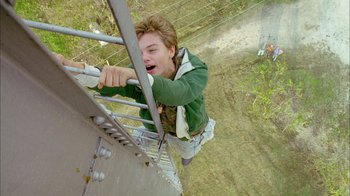 Movie still from “What's Eating Gilbert Grape” (1993), directed by Lasse Hallström – A man hanging from a metal pole on top of a building; Medium shot, Overhead angle