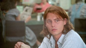 Movie still from “What's Eating Gilbert Grape” (1993), directed by Lasse Hallström – A man with long red hair sitting at a table with a cup of coffee; Close Up shot, Low angle