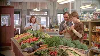 Movie still from “What's Eating Gilbert Grape” (1993), directed by Lasse Hallström – A man and a woman and a child in front of a table of vegetables; Medium shot, Over the shoulder angle