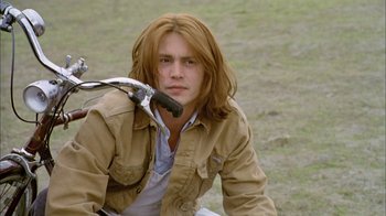 Movie still from “What's Eating Gilbert Grape” (1993), directed by Lasse Hallström – A man with long red hair sitting on the ground; Medium shot, High angle