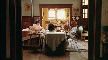 Movie still from “What's Eating Gilbert Grape” (1993), directed by Lasse Hallström – A group of people sitting around a table in a living room; Wide shot, High angle