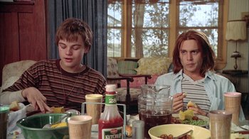 Movie still from “What's Eating Gilbert Grape” (1993), directed by Lasse Hallström – Two young men sitting at a dinner table eating food; Medium shot, Low angle