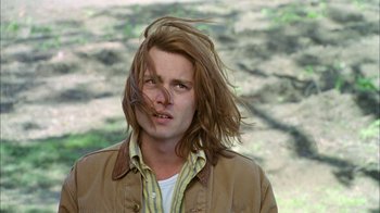 Movie still from “What's Eating Gilbert Grape” (1993), directed by Lasse Hallström – A man with long brown hair is standing in the grass; Close Up shot, Low angle