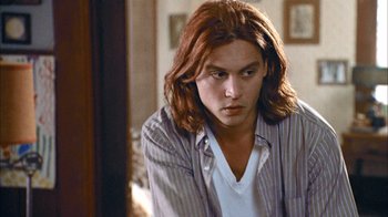 Movie still from “What's Eating Gilbert Grape” (1993), directed by Lasse Hallström – A man with long red hair sitting in a living room; Close Up shot, Over the shoulder angle