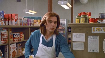 Movie still from “What's Eating Gilbert Grape” (1993), directed by Lasse Hallström – A man with long red hair wearing an apron in a grocery store; Medium shot, Low angle