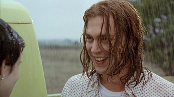Movie still from “What's Eating Gilbert Grape” (1993), directed by Lasse Hallström – A man with long red hair is smiling in the rain; Close Up shot, Over the shoulder angle