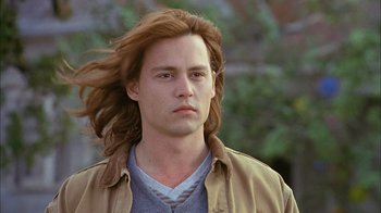 Movie still from “What's Eating Gilbert Grape” (1993), directed by Lasse Hallström – A man with long red hair is standing in front of a tree; Close Up shot, Low angle