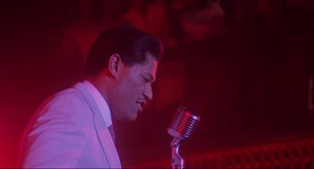 Movie still from “What's Love Got to Do with It” (1993), directed by Brian Gibson – A man in a white suit is singing into a microphone; Close Up shot, Low angle