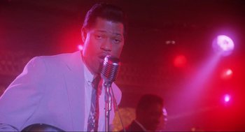 Movie still from “What's Love Got to Do with It” (1993), directed by Brian Gibson – A man in a white suit is singing into a microphone; Close Up shot, Low angle