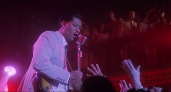 Movie still from “What's Love Got to Do with It” (1993), directed by Brian Gibson – A man singing into a microphone in front of an audience; Medium shot, Low angle