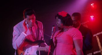 Movie still from “What's Love Got to Do with It” (1993), directed by Brian Gibson – A man and a woman sing into microphones; Medium shot, Low angle