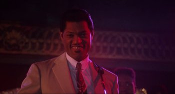 Movie still from “What's Love Got to Do with It” (1993), directed by Brian Gibson – A man wearing a suit and tie smiling for the camera; Close Up shot, Low angle