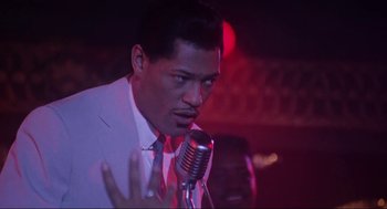 Movie still from “What's Love Got to Do with It” (1993), directed by Brian Gibson – A man in a white suit is singing into a microphone; Close Up shot, Low angle