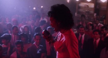 Movie still from “What's Love Got to Do with It” (1993), directed by Brian Gibson – An african american woman singing into a microphone in front of a crowd; Medium shot, Low angle