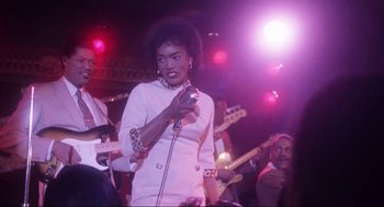 Movie still from “What's Love Got to Do with It” (1993), directed by Brian Gibson – A woman holding a microphone while standing in front of a band; Medium shot, Low angle