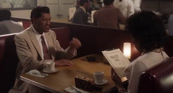 Movie still from “What's Love Got to Do with It” (1993), directed by Brian Gibson – Two people sitting at a table in a restaurant; Medium shot, Over the shoulder angle