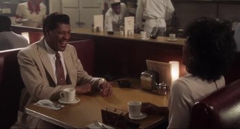 Movie still from “What's Love Got to Do with It” (1993), directed by Brian Gibson – Two men sitting at a table in a restaurant; Medium shot, Over the shoulder angle