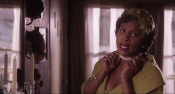 Movie still from “What's Love Got to Do with It” (1993), directed by Brian Gibson – An older woman putting on a necklace in a room; Close Up shot, Over the shoulder angle