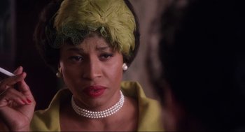 Movie still from “What's Love Got to Do with It” (1993), directed by Brian Gibson – An older woman wearing a yellow dress and a green hat; Close Up shot, Over the shoulder angle