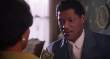 Movie still from “What's Love Got to Do with It” (1993), directed by Brian Gibson – A man in a suit and tie holding money; Close Up shot, Over the shoulder angle