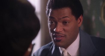 Movie still from “What's Love Got to Do with It” (1993), directed by Brian Gibson – A person wearing a suit and tie; Close Up shot, Over the shoulder angle