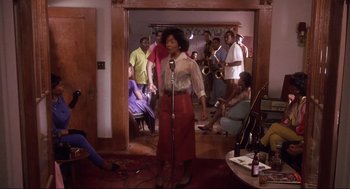 Movie still from “What's Love Got to Do with It” (1993), directed by Brian Gibson – A group of people standing around a room with a microphone; Wide shot, High angle