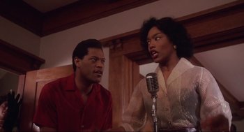 Movie still from “What's Love Got to Do with It” (1993), directed by Brian Gibson – A man and a woman sing into microphones in front of each other; Medium shot, Low angle