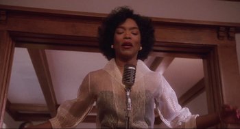 Movie still from “What's Love Got to Do with It” (1993), directed by Brian Gibson – A woman is singing into a microphone in front of a wooden wall; Medium shot, Low angle