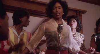 Movie still from “What's Love Got to Do with It” (1993), directed by Brian Gibson – A group of people that are standing in front of a microphone; Medium shot, Low angle