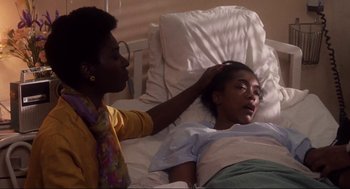 Movie still from “What's Love Got to Do with It” (1993), directed by Brian Gibson – A person laying in a hospital bed with a woman; Medium shot, High angle