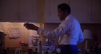Movie still from “What's Love Got to Do with It” (1993), directed by Brian Gibson – A man in a white shirt is playing a video game in a kitchen; Medium shot, Low angle