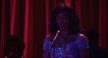 Movie still from “What's Love Got to Do with It” (1993), directed by Brian Gibson – A woman in a blue dress holding a microphone in front of a red curtain; Medium shot, Low angle