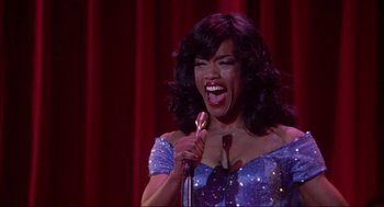 Movie still from “What's Love Got to Do with It” (1993), directed by Brian Gibson – A woman in a blue dress holding a gold microphone; Medium shot, Low angle