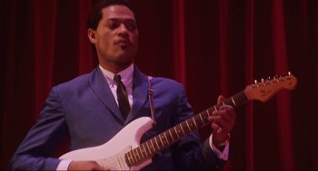 Movie still from “What's Love Got to Do with It” (1993), directed by Brian Gibson – A man in a suit and tie playing a guitar; Close Up shot, Low angle