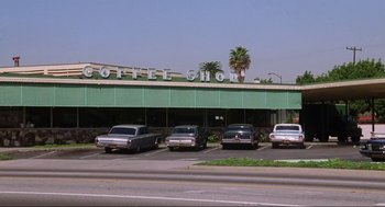 Movie still from “What's Love Got to Do with It” (1993), directed by Brian Gibson – A group of cars parked in front of a coffee shop; Extreme Wide shot, High angle
