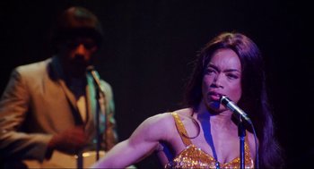 Movie still from “What's Love Got to Do with It” (1993), directed by Brian Gibson – A woman singing into a microphone on a stage; Close Up shot, Low angle