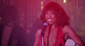 Movie still from “What's Love Got to Do with It” (1993), directed by Brian Gibson – A woman in a sequined red dress holding a microphone and smiling; Close Up shot, Low angle