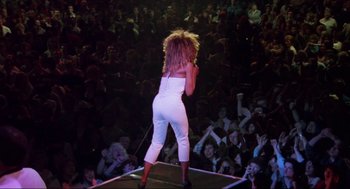 Movie still from “What's Love Got to Do with It” (1993), directed by Brian Gibson – A woman in a white outfit on a stage with a crowd of people; Wide shot, High angle