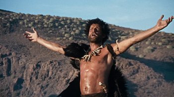 Movie still from “When Dinosaurs Ruled the Earth” (1970), directed by Val Guest – A man with a bare chest and bare torso is standing with his arms outstretched; Medium shot, Low angle