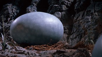 Movie still from “When Dinosaurs Ruled the Earth” (1970), directed by Val Guest – An ostrich egg laying in the dirt next to rocks; Close Up shot, High angle