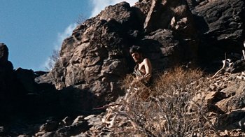 Movie still from “When Dinosaurs Ruled the Earth” (1970), directed by Val Guest – A man standing on top of a hill next to rocks; Wide shot, Low angle